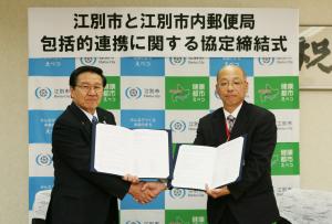 協定書を手に握手する三好市長と本田局長